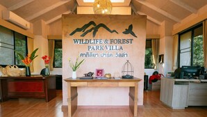 Un mostrador de recepción con un letrero que dice Wildlife & Forest Parkvilla, techo de madera y un amplio ventanal.