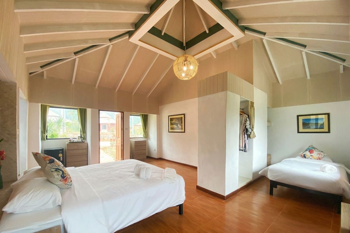 A spacious bedroom with two beds, wooden flooring, a ceiling with exposed beams, and a large window.