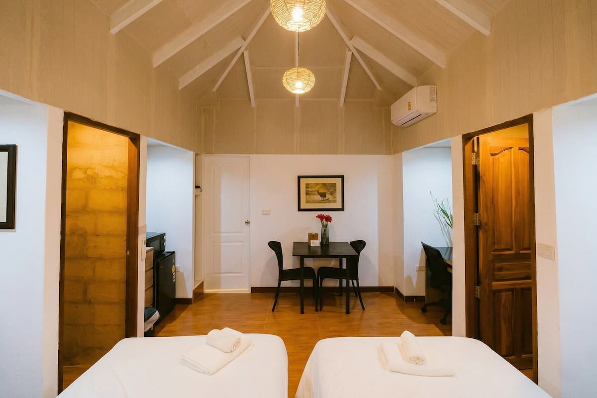 A hotel room with two beds, a dining table, chairs, a painting, and a ceiling light fixture.