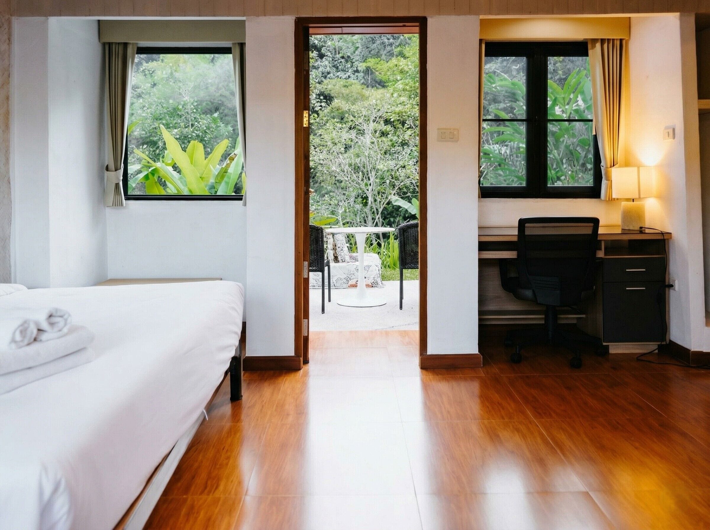 A hotel room with a bed, a desk, and a view of a garden through an open door.
