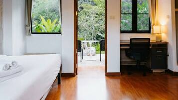 A hotel room with a bed, a desk, and a view of a garden through an open door.