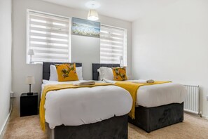 A double bed with a headboard, a bedside table, a lamp, and a window with blinds. - Free parking, private garden and Elizabeth Line at your door (Greater London)