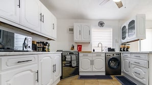 Een moderne keuken met witte kasten, een ingebouwde oven, een wasmachine en een magnetron.