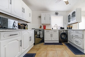 A modern kitchen with white cabinetry, a built-in oven, a washing machine, and a microwave. - Free parking, private garden and Elizabeth Line at your door (Greater London)
