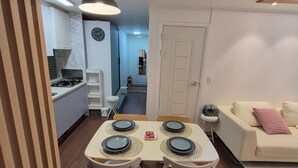 Ein Essbereich mit Tisch für vier Personen, eine Küche im Hintergrund und eine Wohnbereich mit Sofa und einem kleinen Beistelltisch.