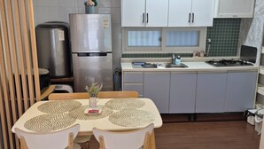 Eine moderne Küche mit weißen Schränken, einem Edelstahlkühlschrank, einem Gasherd und einem Essbereich mit Tisch und Stühlen.