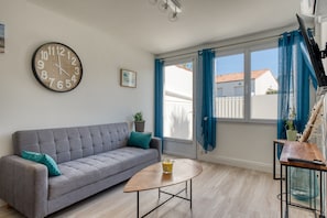 Un salon avec un canapé, une table basse, une horloge murale et une fenêtre avec des rideaux.