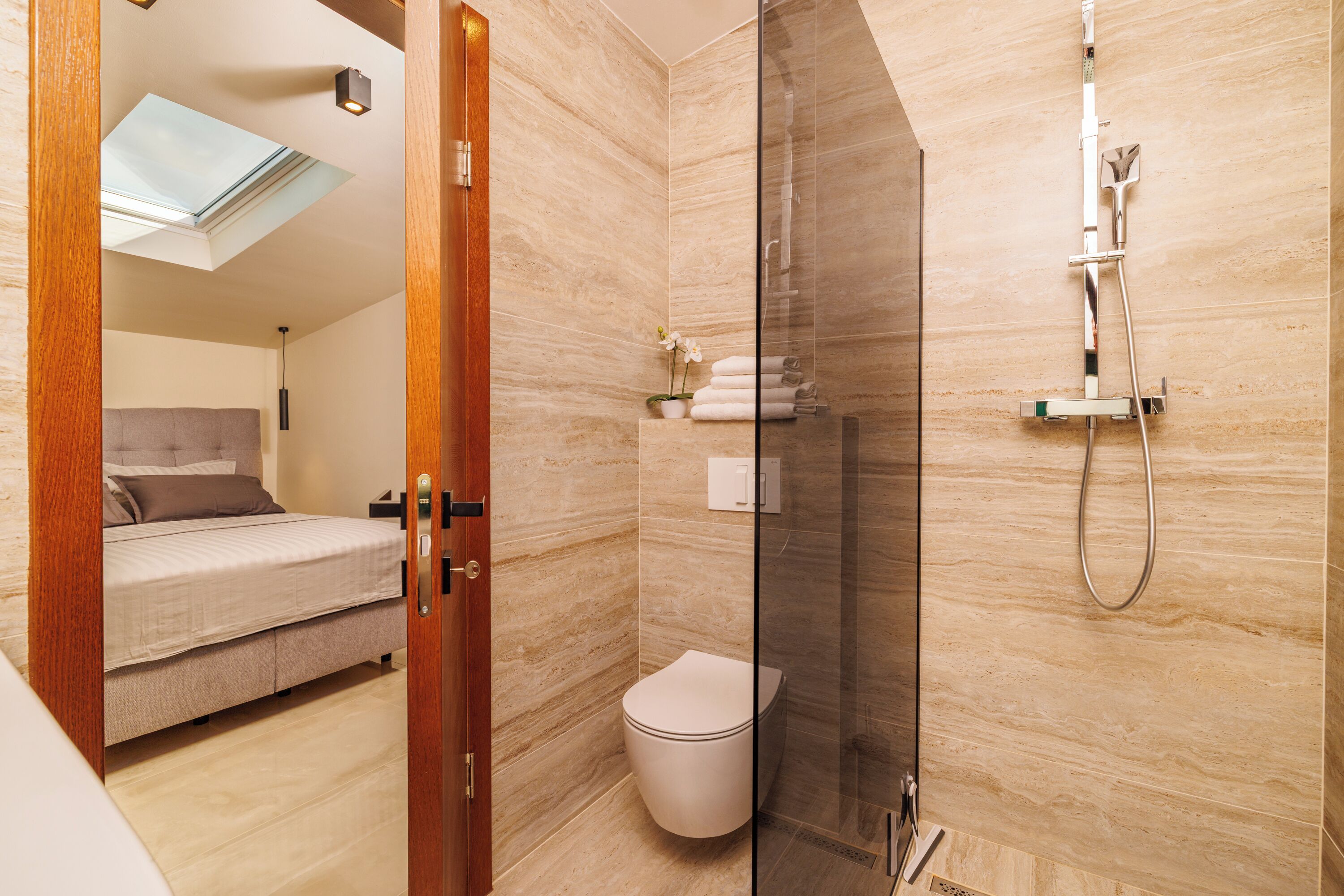 Ein modernes Badezimmer mit Duschkabine aus Glas, Toilette und einem Bett im angrenzenden Raum.