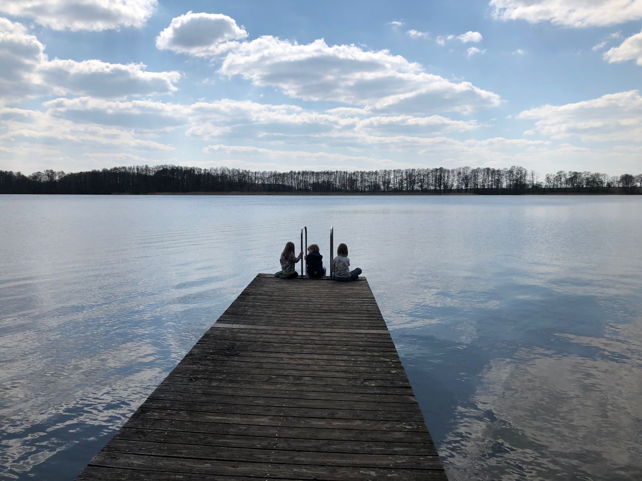 A wooden pier extending into calm water with a clear sky above.