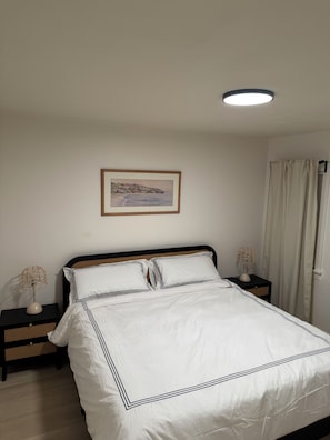 A neatly made bed with white bedding and black trim, a framed picture on the wall, and a ceiling light. - Wrigley Spanish Bungalow • 3 Bed • 5 Min Downtown (Long Beach)
