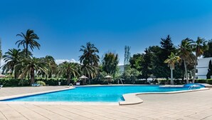 Ein Swimmingpool mit Liegestühlen, Palmen und blauem Himmel.