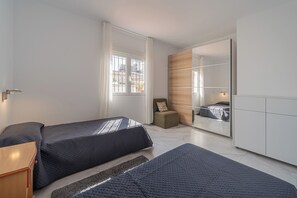 Quarto moderno com duas camas, um espaço de estar pequeno e um espelho grande.