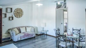 A living room with a sofa, a dining table with chairs, a round clock on the wall, and a hanging light fixture. - Blue Nest Ottava - A few minutes from Sassari (Ottava)