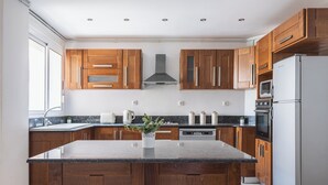 A modern kitchen with wooden cabinets, a central island, stainless steel appliances, and a window providing natural light.