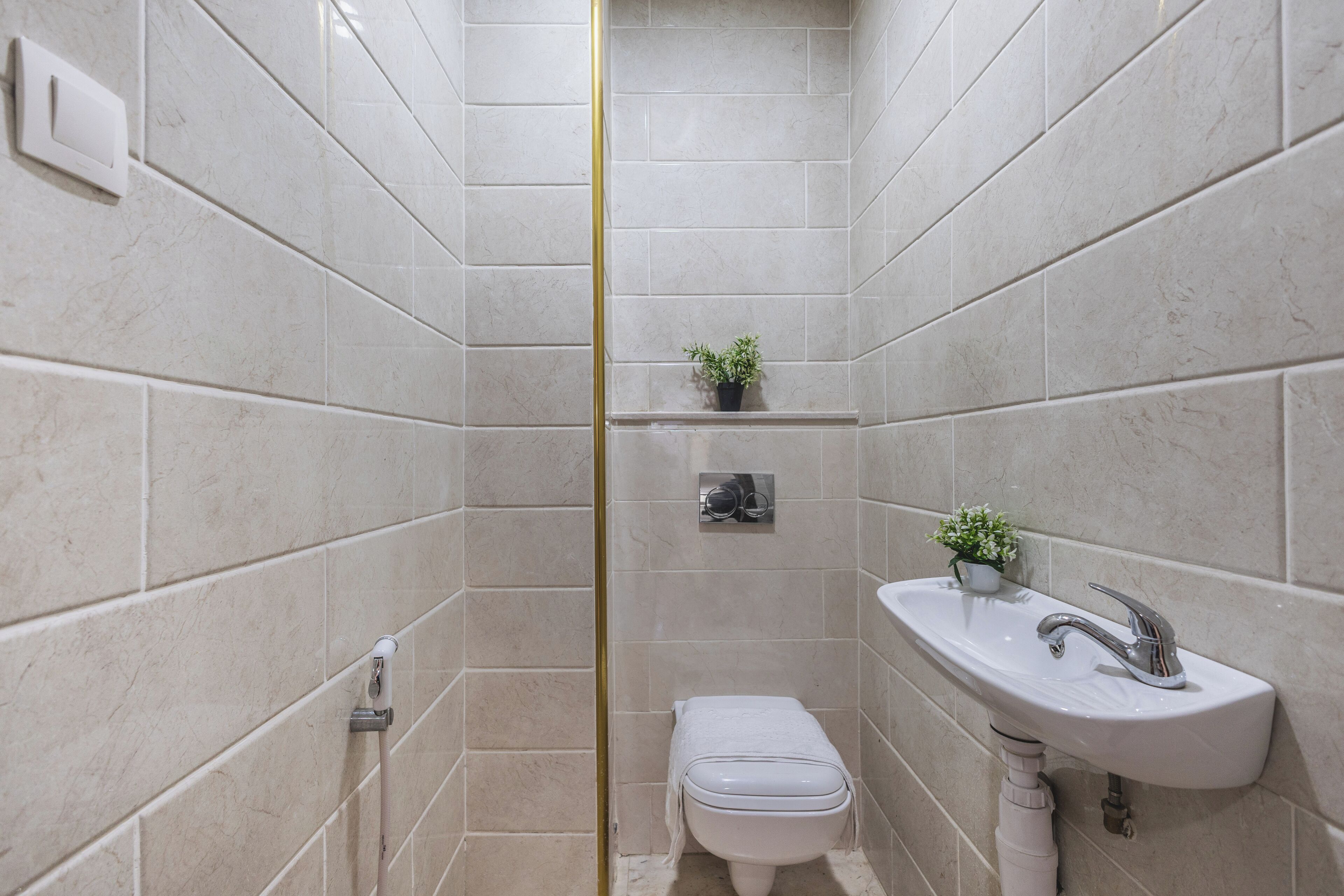 Une salle de bain équipée de toilettes, d’un lavabo, d’une douche et d’une petite étagère sur laquelle est posée une plante.