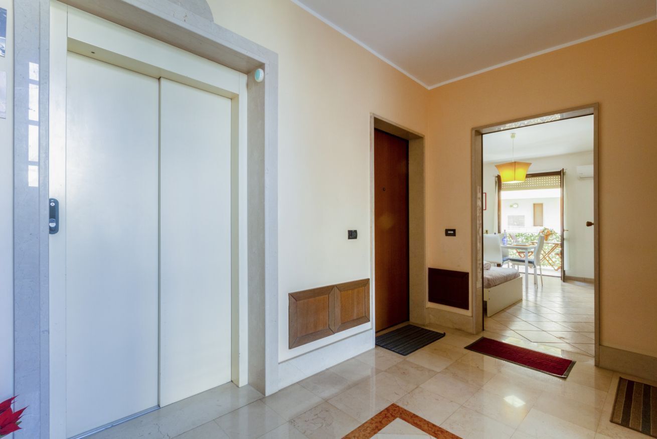 Corredor de hotel com porta fechada, um pequeno hall de entrada e vista para um quarto com varanda.