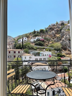 A balcony with a round table and wooden chairs, overlooking a hillside with white buildings and greenery. - Siena House Hydra - Renovated in 2026 (Idra)