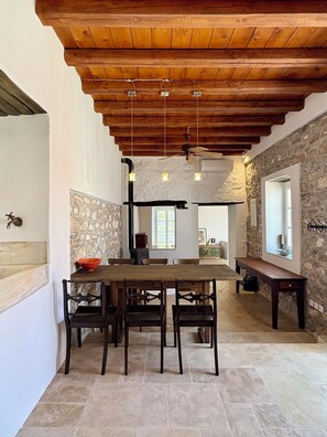 A dining area with a wooden table, chairs, and a stone wall. - Siena House Hydra - Renovated in 2026 (Idra)