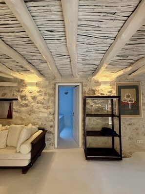 A room with a stone wall, a white sofa, a glass display case, and a framed picture on the wall. - Siena House Hydra - Renovated in 2026 (Idra)
