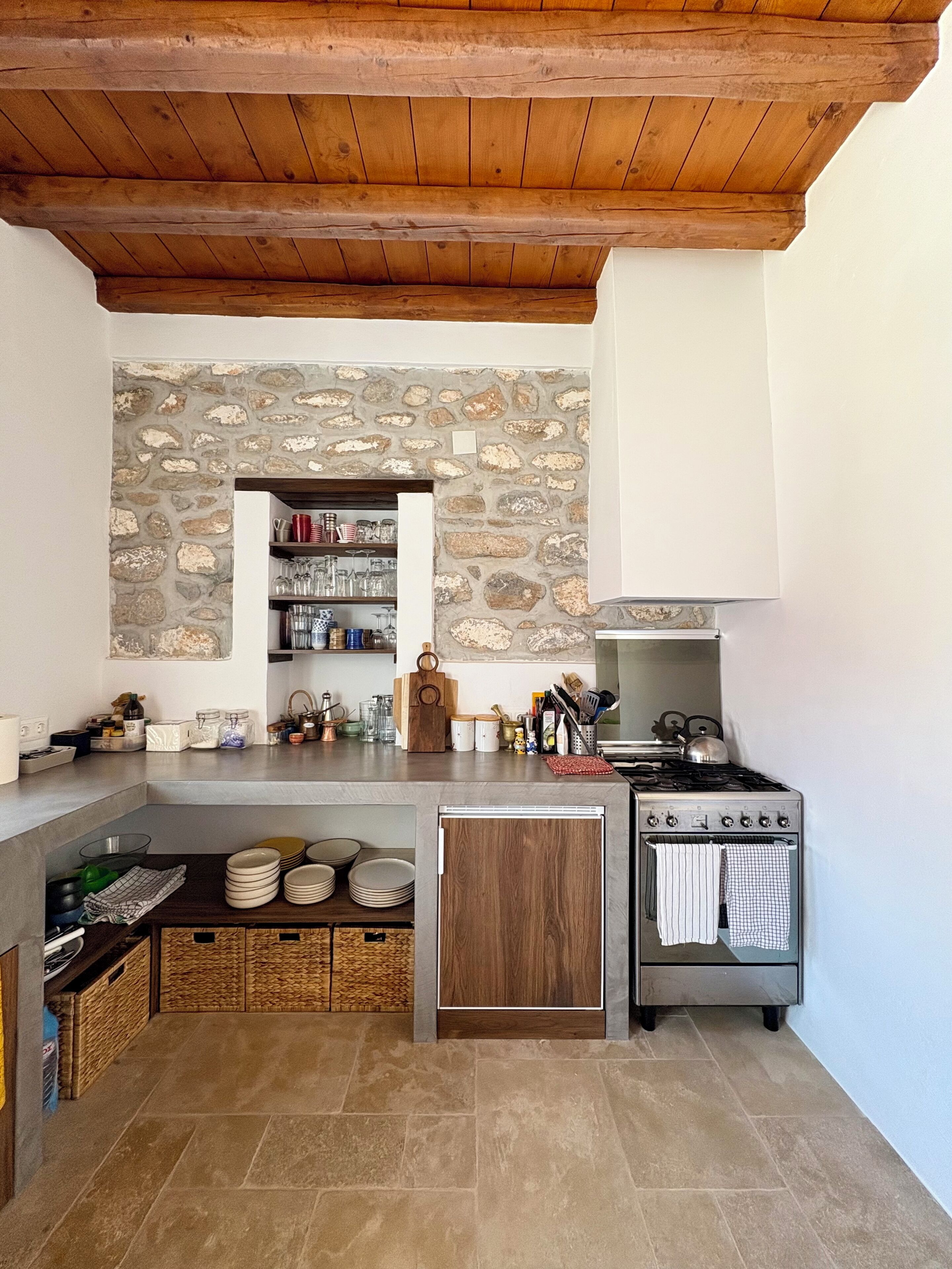A kitchen with a stone wall, wooden ceiling, and a built-in oven.