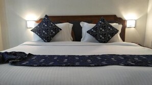 Una cama bien hecha con un edredón estampado, dos almohadas decorativas y dos lámparas fijadas a la pared.