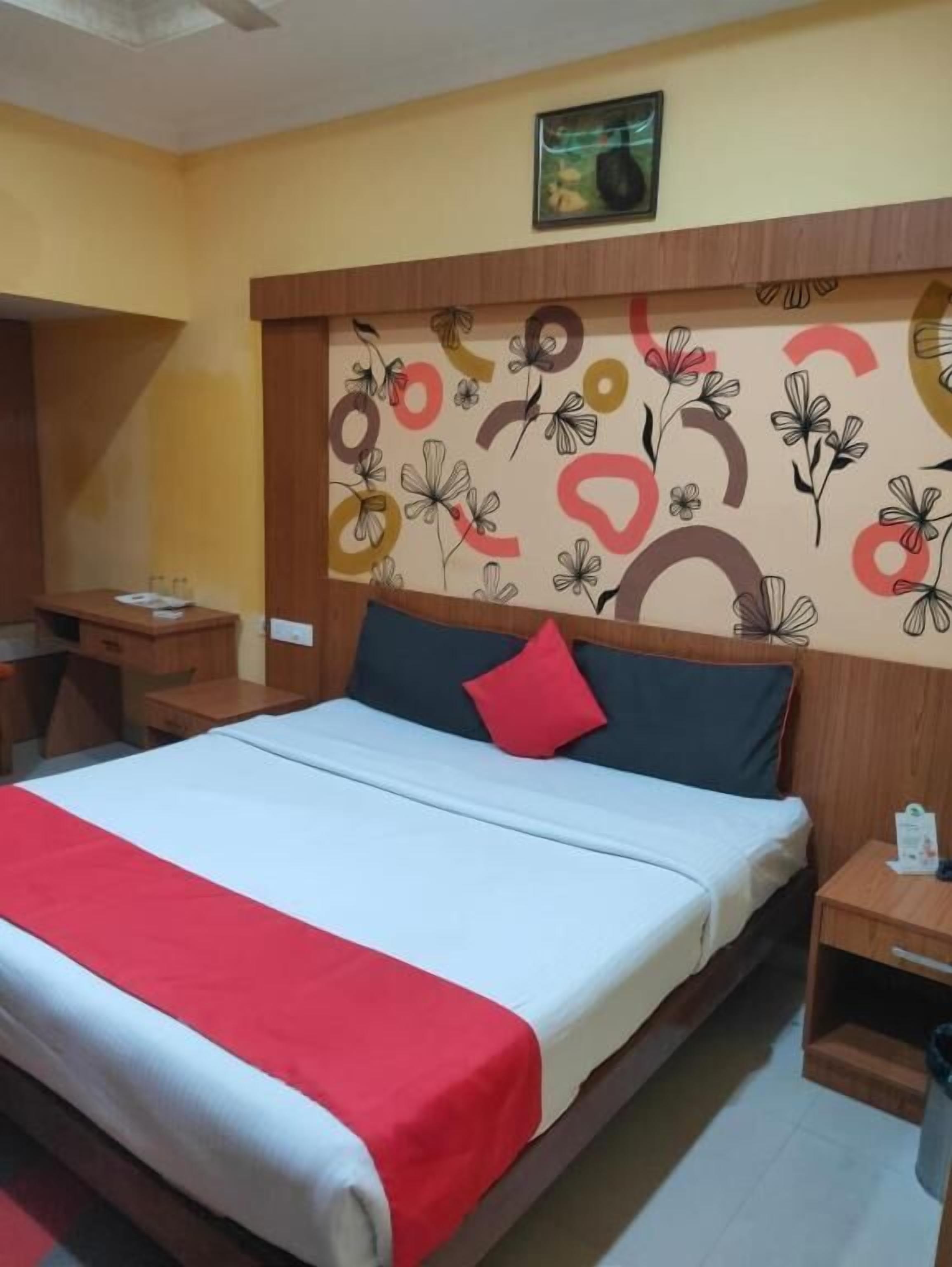 A hotel room with a bed, a desk, a chair, and a wall with a floral and circular pattern.