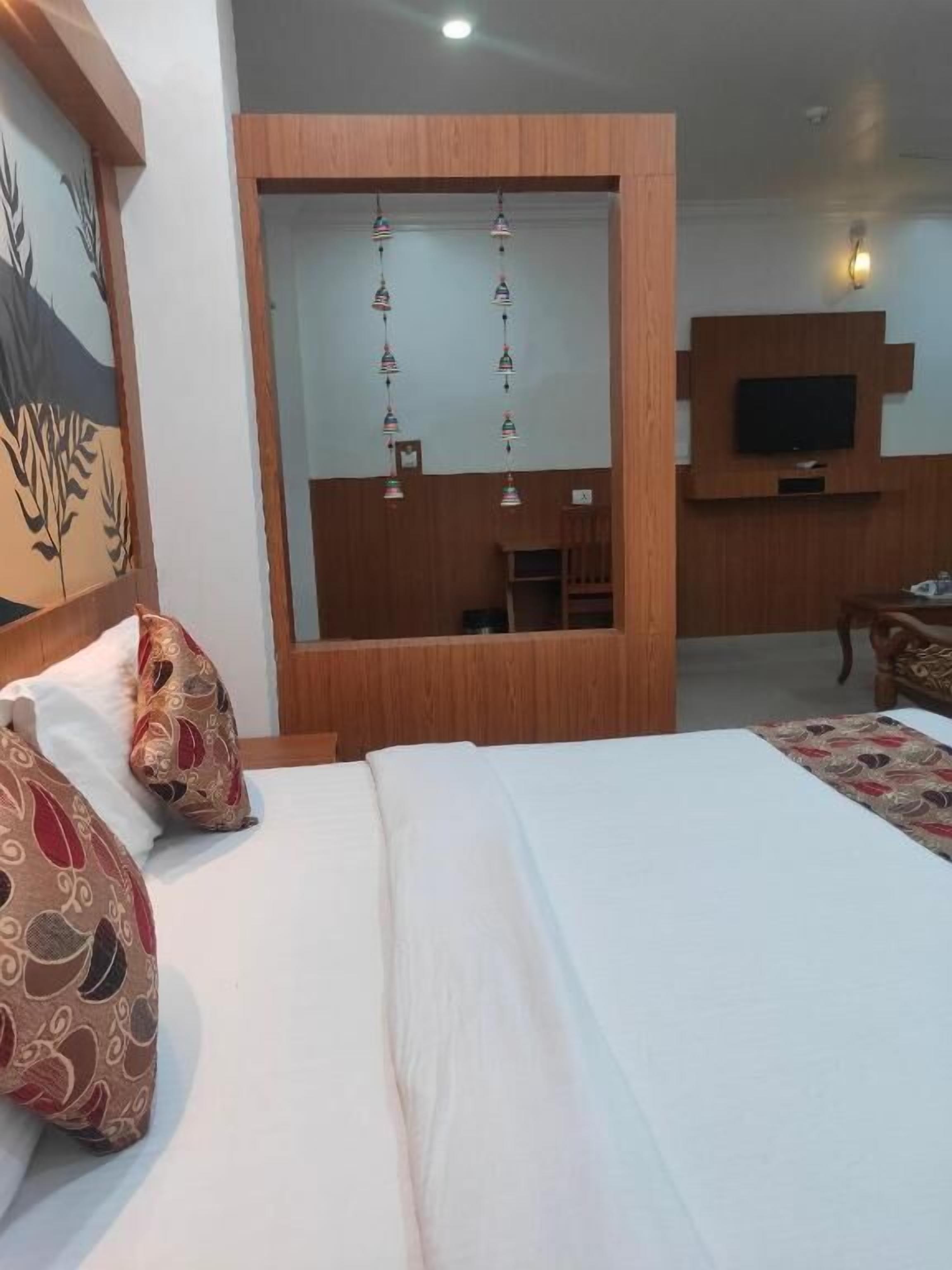 Habitació d'hotel amb un llit, almoines, un televisor, un moble de paret de fusta i una làmpada penjant.
