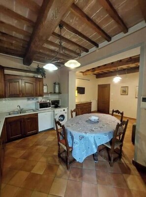 A kitchen with wooden cabinets, a dining table with chairs, a washing machine, and a ceiling fan. - The Writing Desk (Scarperia e San Piero)