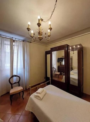 A bedroom with a bed, a chair, a mirror, and a chandelier. - The Writing Desk (Scarperia e San Piero)