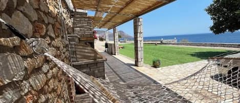 Un edificio de piedra con un espacio al aire libre cubierto, un césped y vistas al mar.