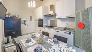 Una cocina moderna con armarios blancos, una estufa a gas y un lavamanos. Hay una mesa de comedor puesta con platos y tazas.