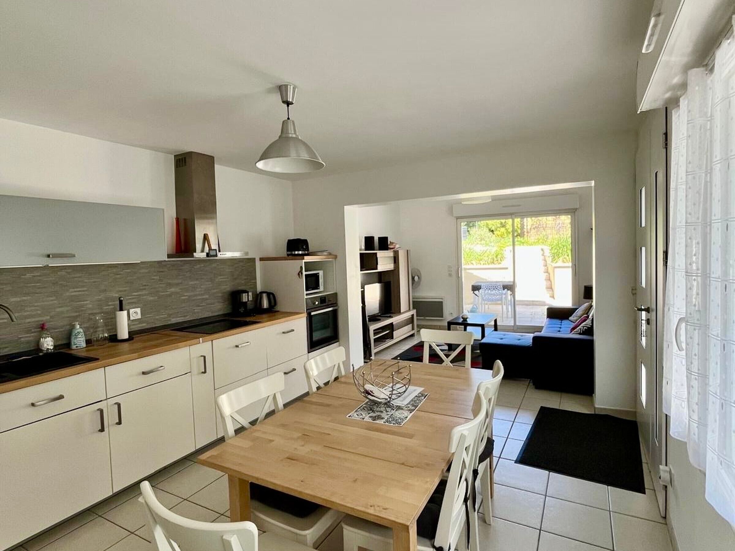 A modern kitchen with white cabinets, a wooden dining table, and a view to a patio area.