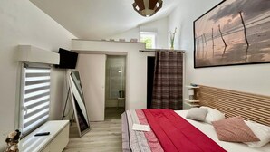 A modern bedroom with a bed, a TV, a window with blinds, a painting, and a ceiling light fixture. - Renovated house with equipped kitchen in La Roche-Posay (La Roche-Posay)