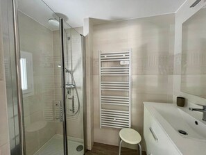 A modern bathroom with a glass-enclosed shower, a white vanity with a mirror, and a towel rack.