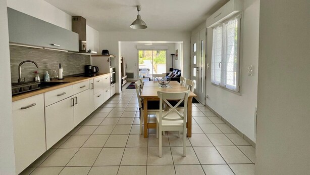 A modern kitchen with white cabinets, a dining table with chairs, and a view to the outside. - Renovated house with equipped kitchen in La Roche-Posay (La Roche-Posay)