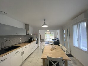 A modern kitchen with white cabinets, a wooden countertop, and a dining area with a table and chairs. - Renovated house with equipped kitchen in La Roche-Posay (La Roche-Posay)