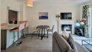 A modern living room with a sofa, a dining table with chairs, a fireplace, and a TV mounted on the wall. - Pinner Gem: Quiet Home with private garden (Pinner)