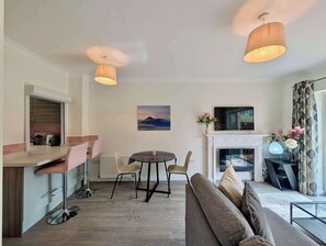 A modern living room with a sofa, a dining table with chairs, a fireplace, and a TV mounted on the wall. - Pinner Gem: Quiet Home with private garden (Pinner)