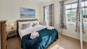 A bedroom with a bed, a nightstand, a lamp, a painting, and patterned curtains. - Pinner Gem: Quiet Home with private garden (Pinner)