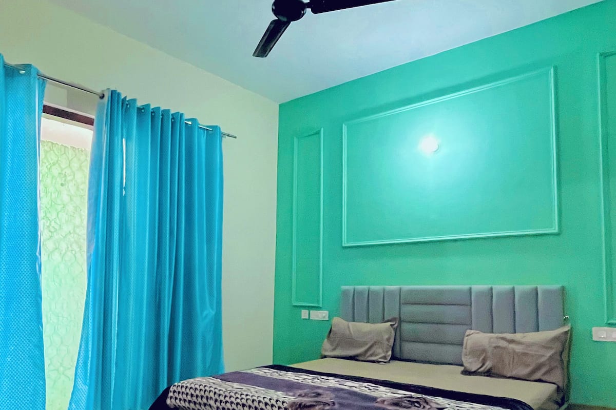 Un dormitorio con cama, ventilador de techo, ventana con cortinas y pared verde.
