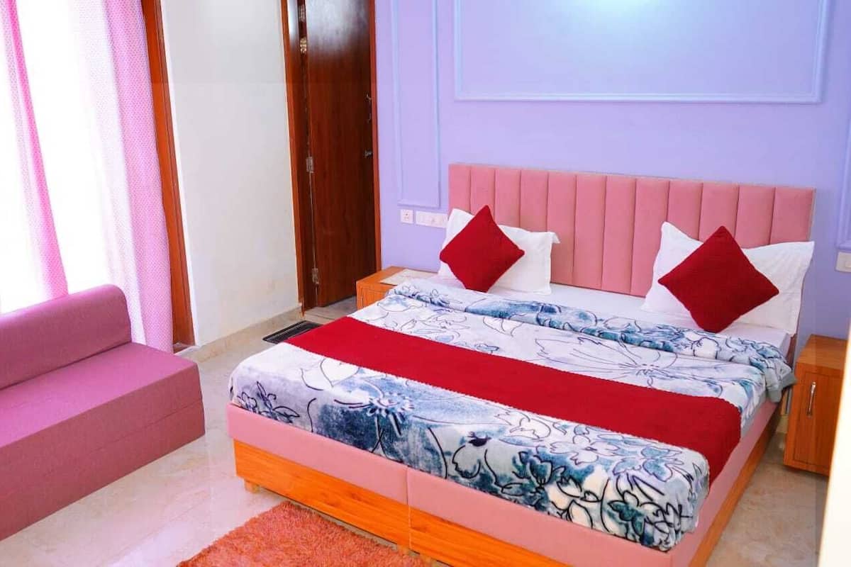 Un dormitorio con cama, sofá rosa y mesita de noche de madera.