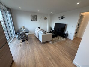 A modern living room with a dining area, a flat-screen TV, and a large window. - Apartment Sleeps 4 With Dishwasher (London)