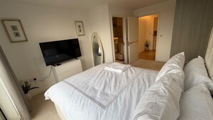 Un dormitorio con cama, televisor, espejo y puerta que da a un baño.