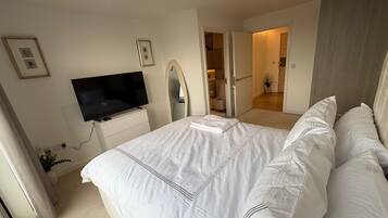 A bedroom with a bed, a television, a mirror, and a door leading to a bathroom.