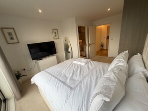 A bedroom with a bed, a television, a mirror, and a door leading to a bathroom. - Apartment Sleeps 4 With Dishwasher (London)