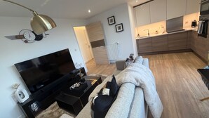 Una sala moderna con televisor de pantalla plana, un sofá, una mesita de centro y una cocina al fondo.
