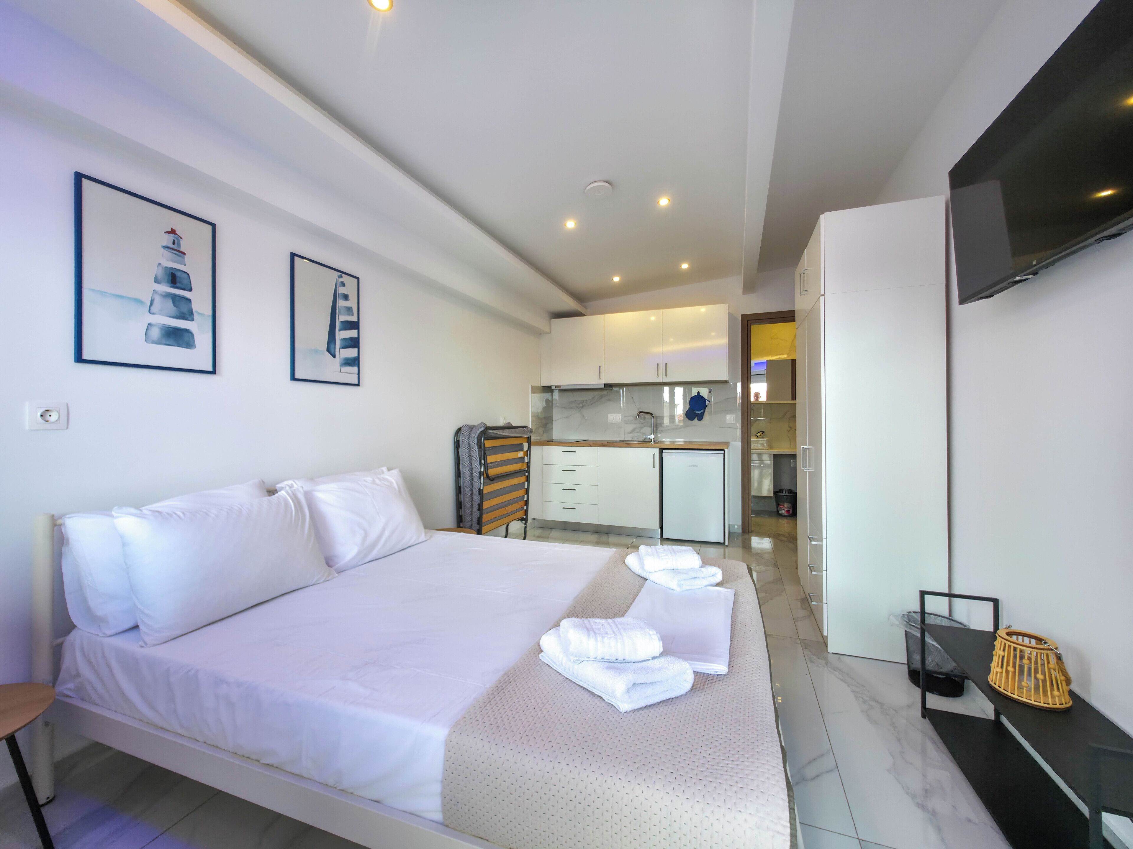 A modern hotel room with a large bed, a small kitchenette, and a TV mounted on the wall.