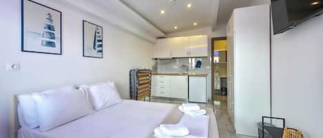 A modern hotel room with a large bed, a small kitchenette, and a TV mounted on the wall.