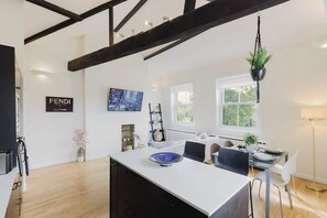 A modern kitchen with a white island, dark wooden beams, and a hanging plant. - Stunning 2BR/2BA w/Views & AC (Greater London)