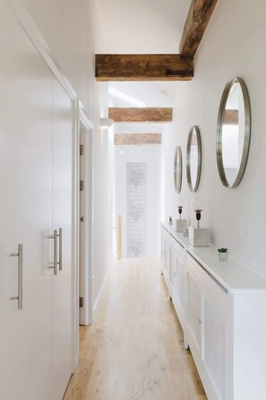 A hallway with white walls, wooden beams, and a white console with mirrors and decorative items. - Stunning 2BR/2BA w/Views & AC (Greater London)